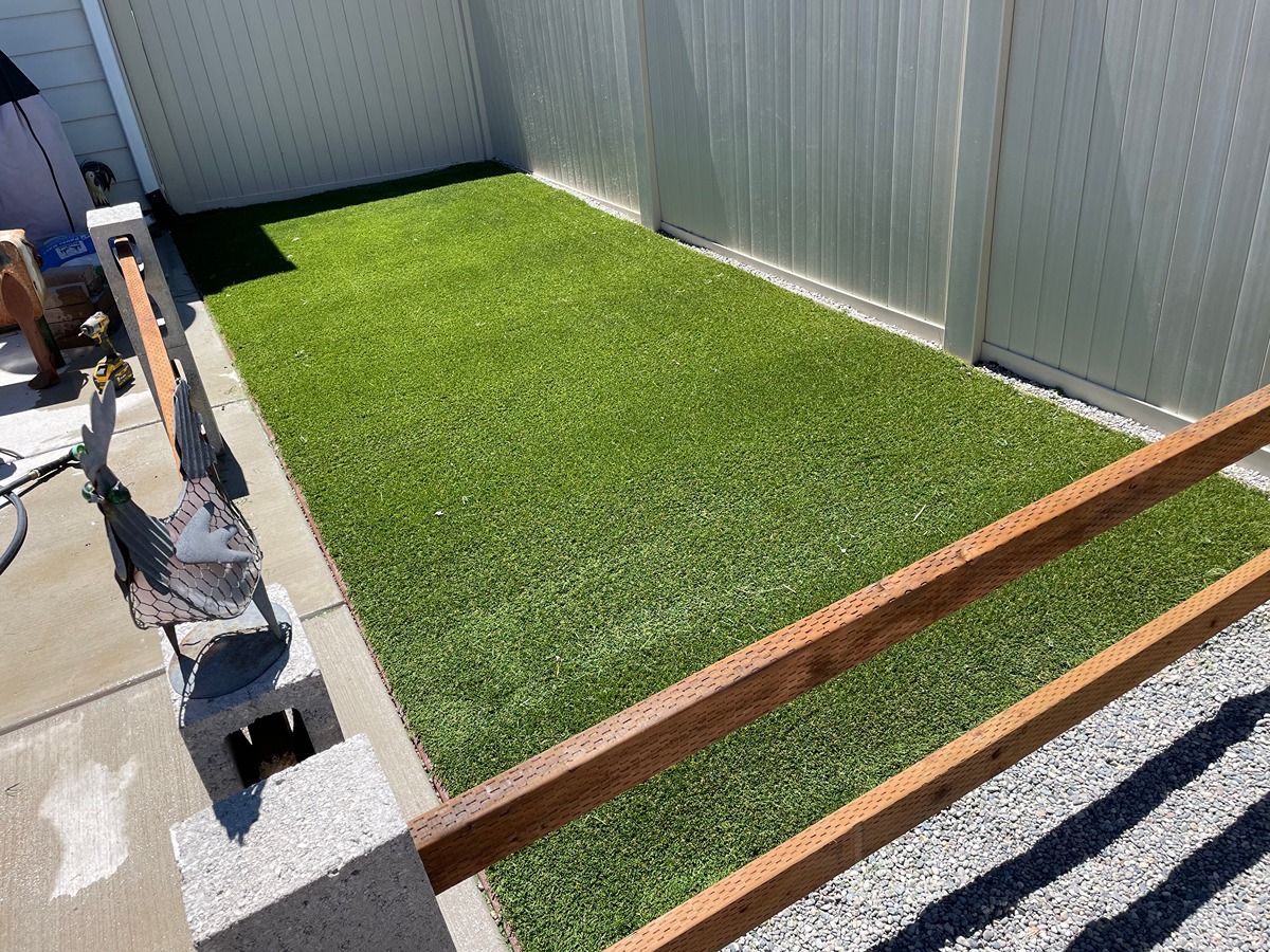 Rectangular green lawn area under construction, bordered by wooden beams beside a corrugated metal fence