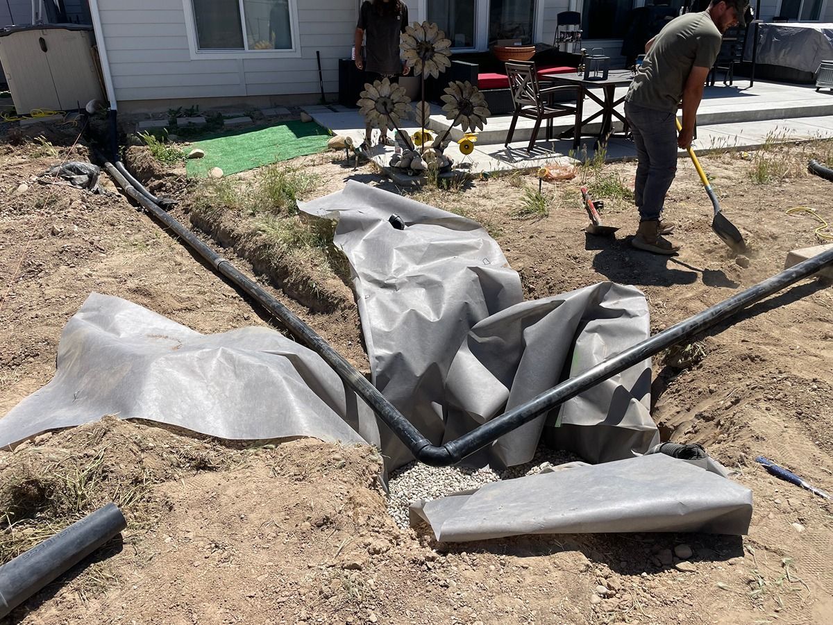 Backyard landscaping work with black tubing, white tarp, and workers near a house