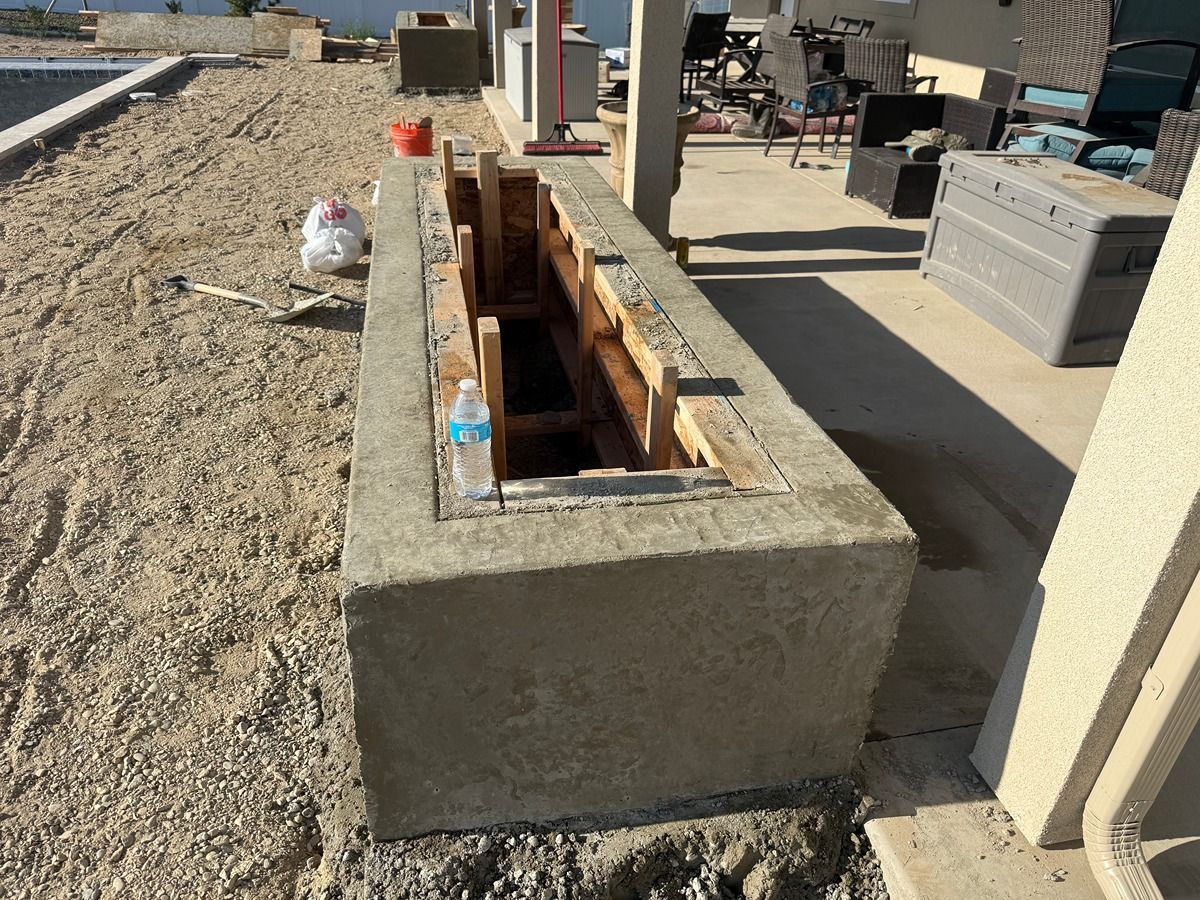 Concrete bench under construction with wooden formwork and tools on a gravel patio.