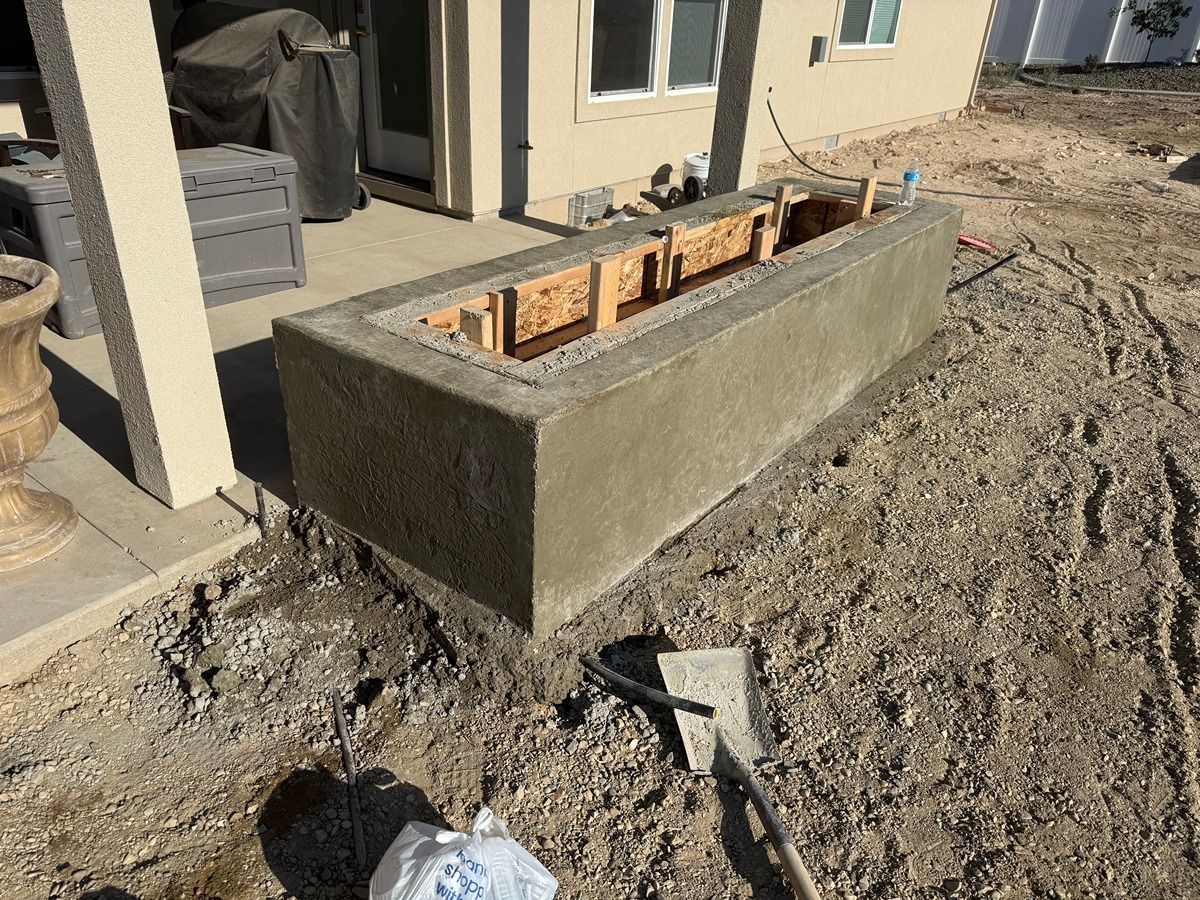 Rectangular concrete planter block at a construction site beside a building, with exposed wood formwork inside.