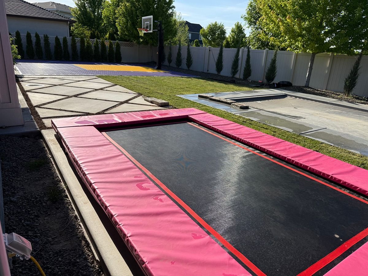 Backyard trampoline with pink padding and black jumping surface beside a house and stone patio
