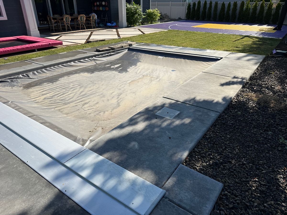 Empty rectangular in-ground pool under construction with concrete edges and surrounding patio.