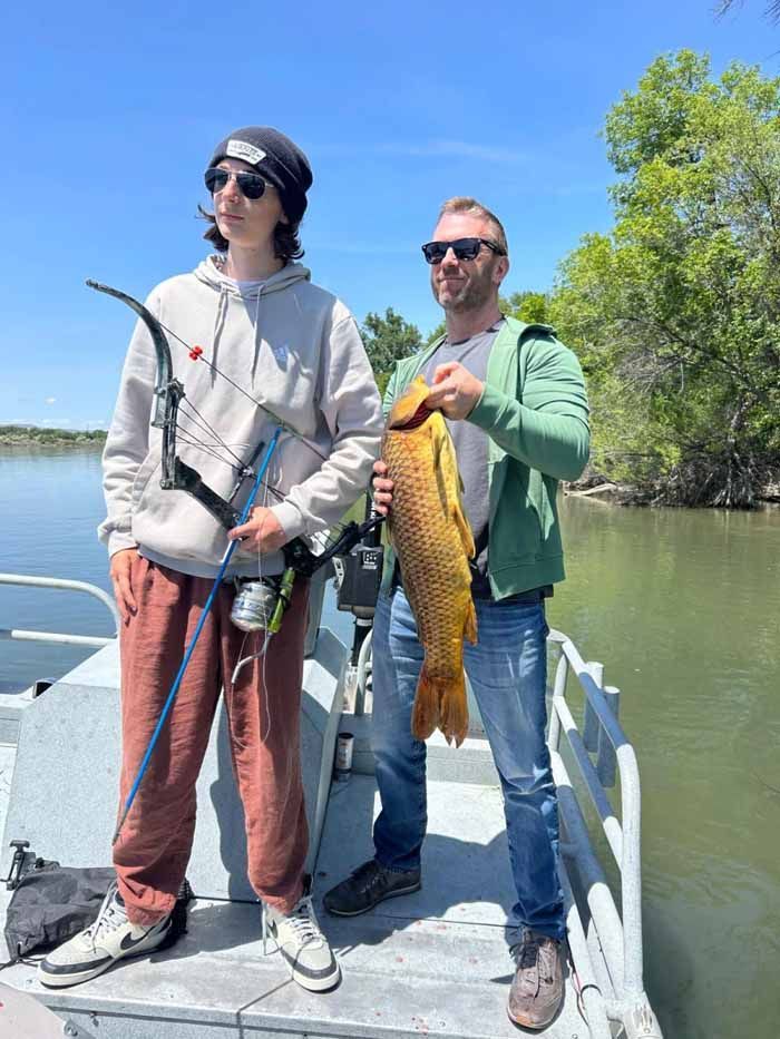 Two men are standing on a boat holding a large fish.