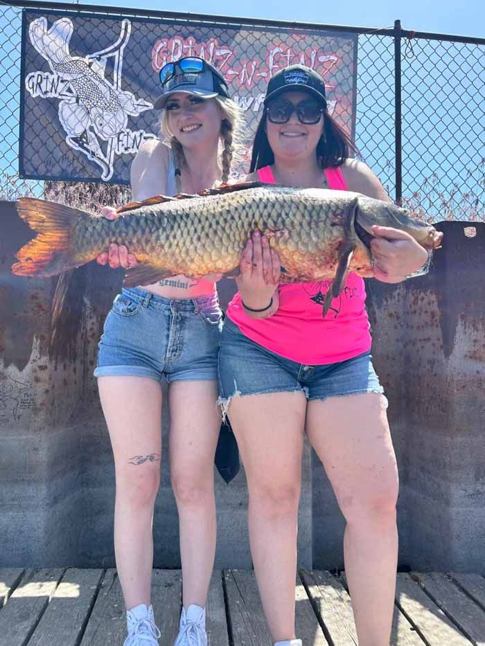 Two women are standing next to each other holding a large fish.