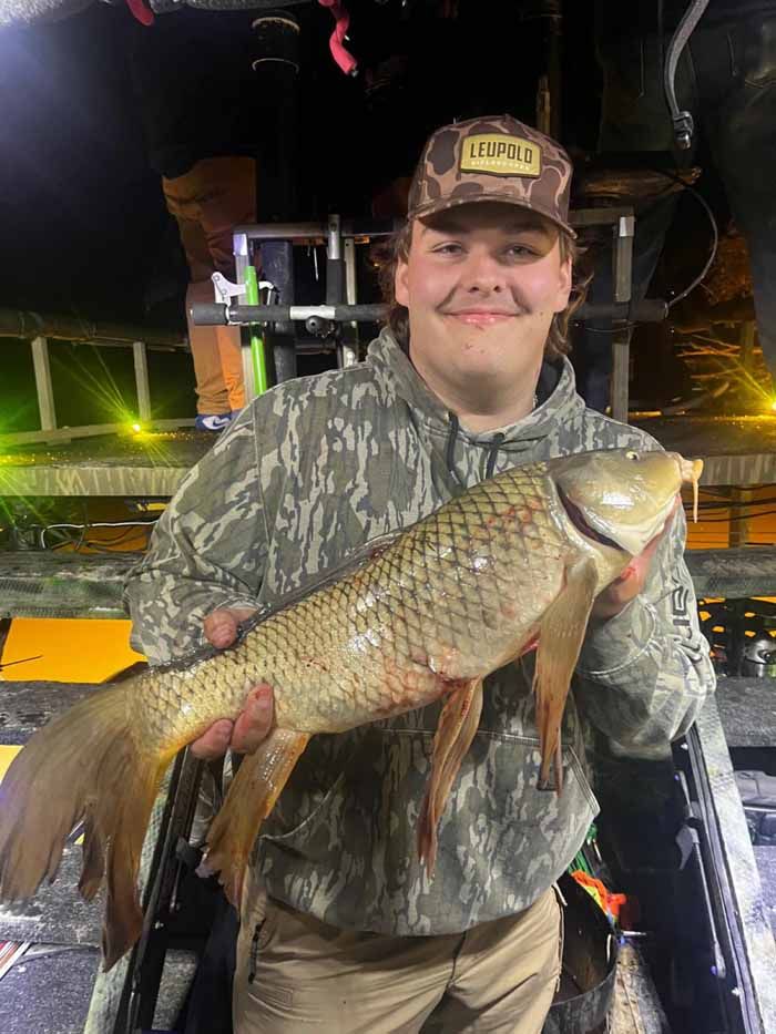 A young man is holding a large fish in his hands.