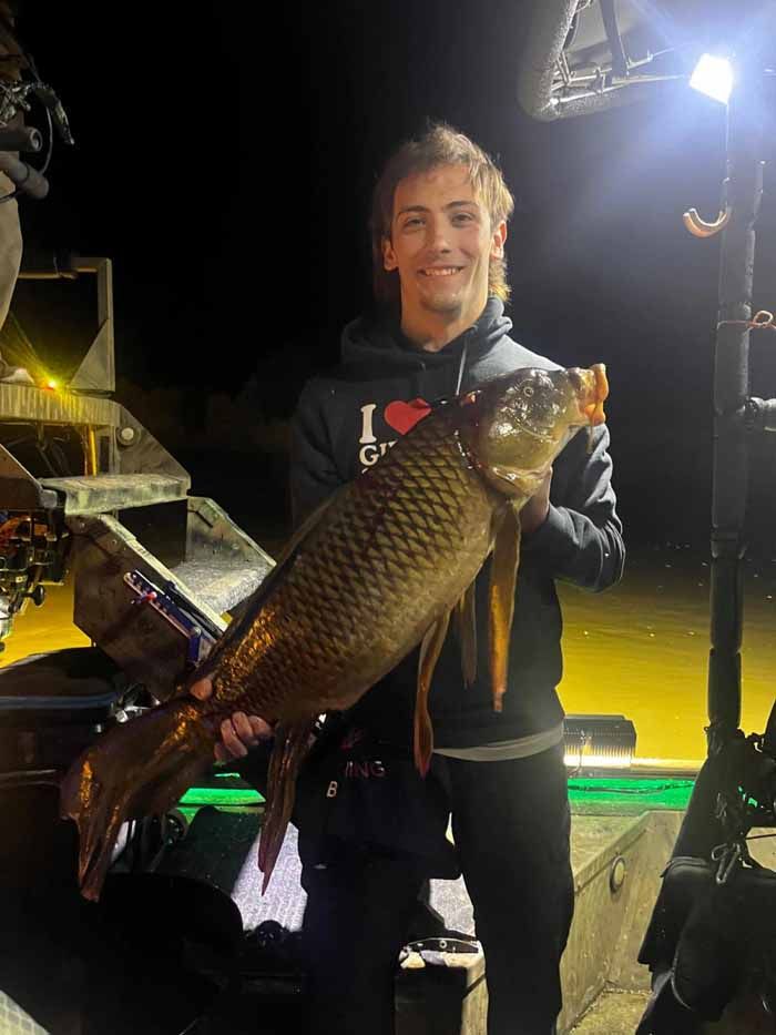 A man in a hoodie that says i love fishing is holding a large fish.