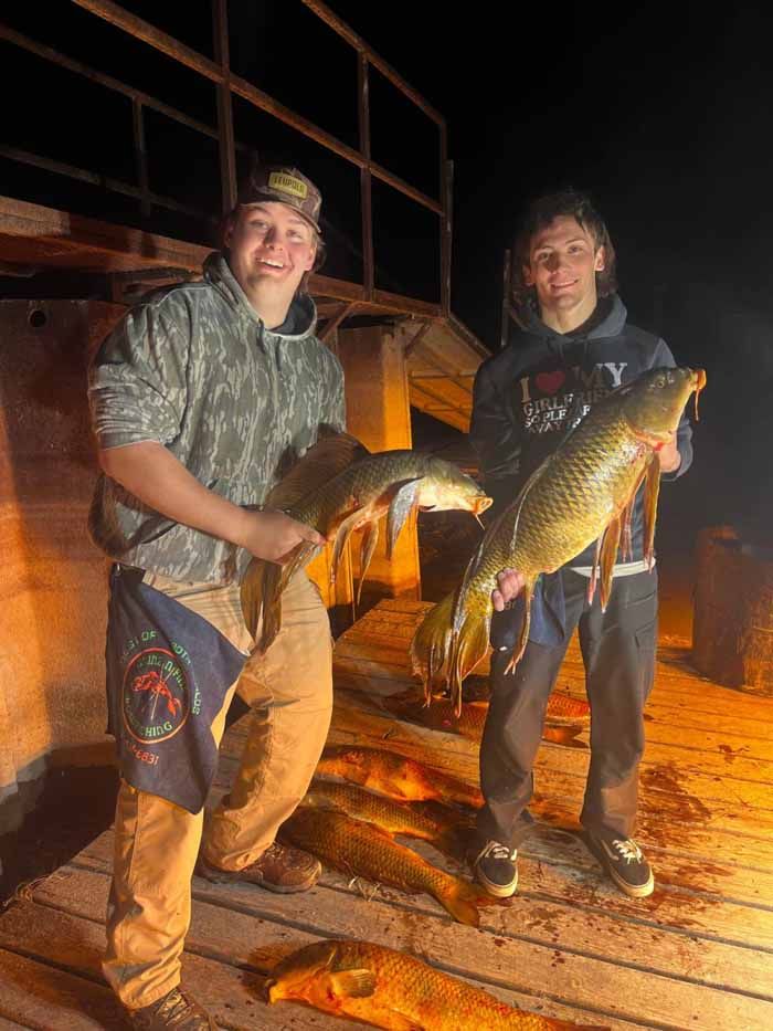Two young men are standing on a dock holding large fish.