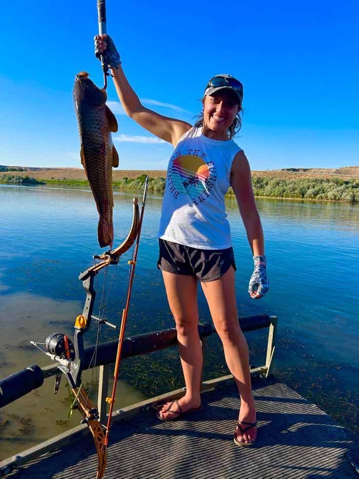A woman is standing on a boat holding a fish in her hand.