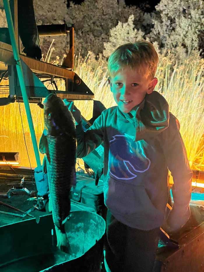 A young boy is holding a large fish in his hands.