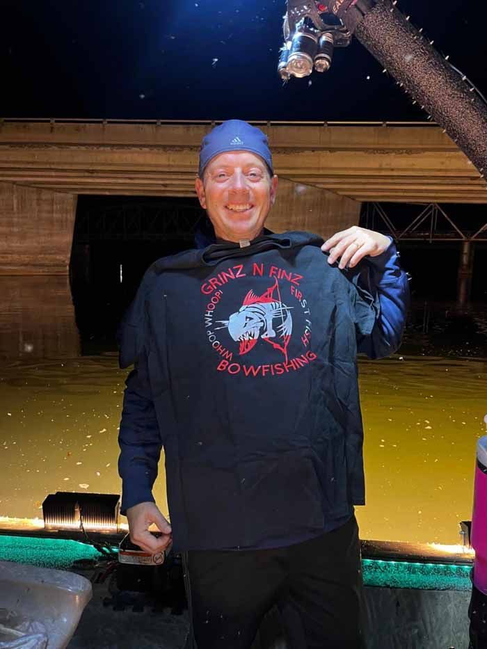 A man is holding a t-shirt over his shoulder in front of a body of water.
