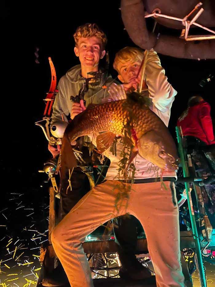 Two men are standing next to each other holding a large fish.