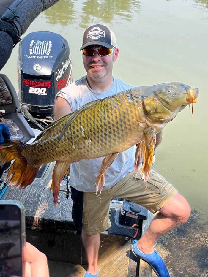 A man is holding a large carp in front of a boat engine.