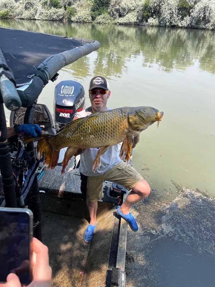 A man is holding a large fish in front of a boat.