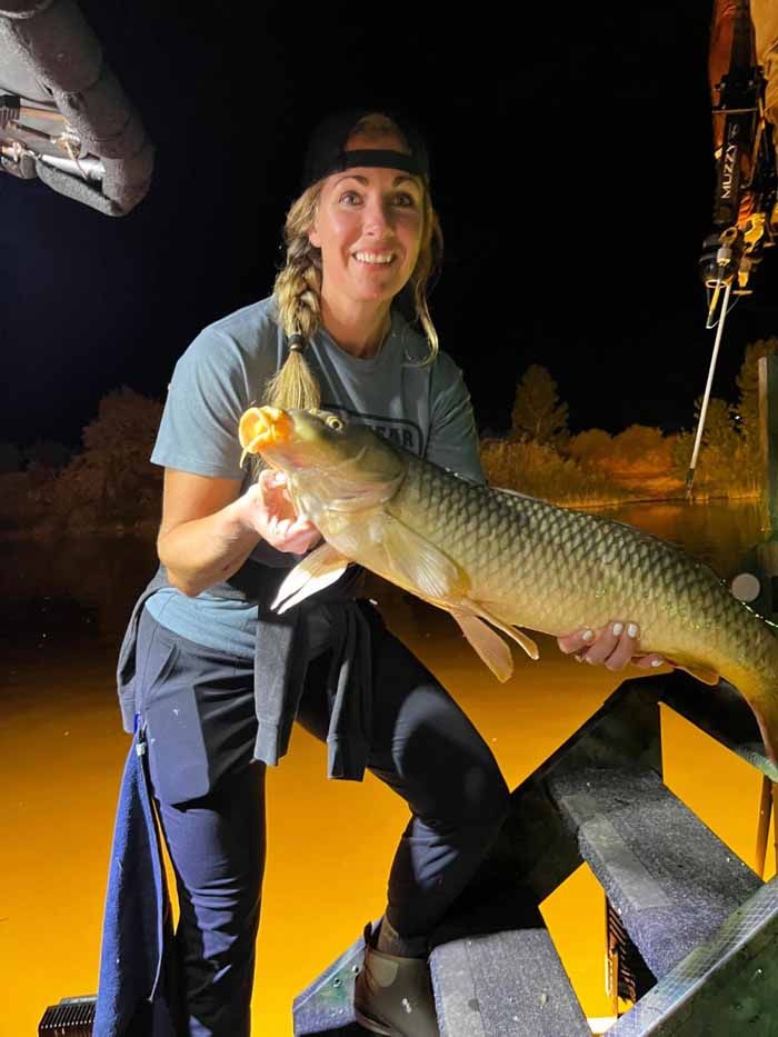 A woman is sitting on a bench holding a large fish.