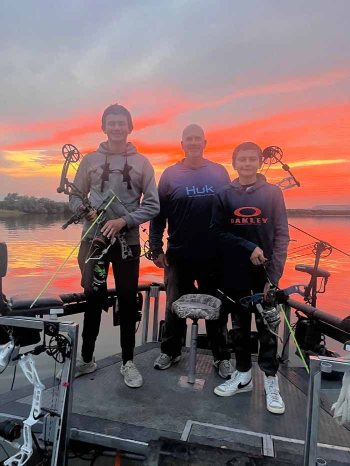 Three men are standing on the deck of a boat holding bows and arrows.