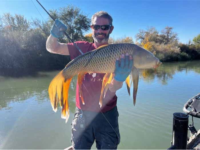 A man is holding a large fish in his hands in front of a body of water.