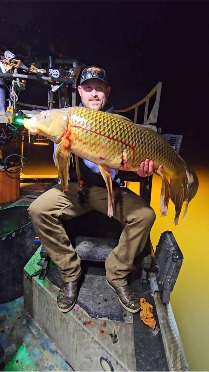 A man is sitting on a boat holding a large carp.