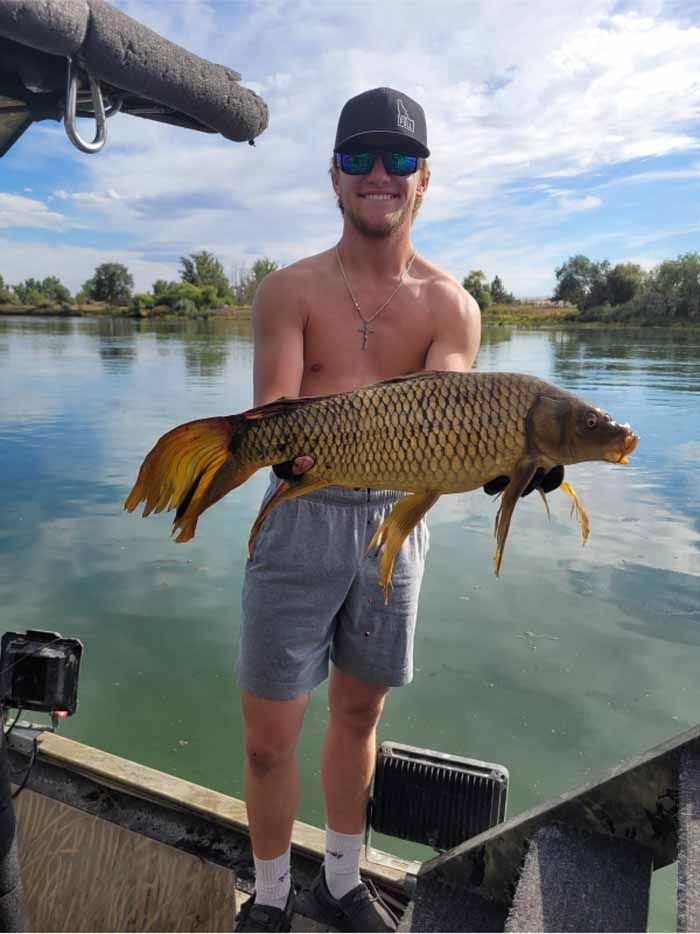 A shirtless man is standing on a boat holding a large fish.
