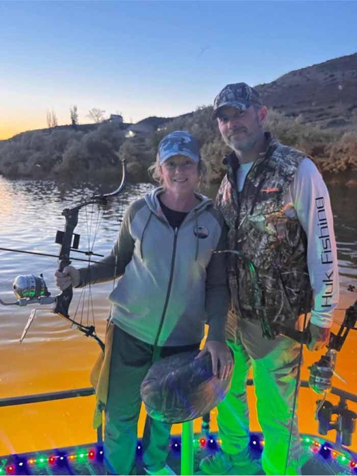 A man and a woman are standing on a boat holding fishing rods and a fish.