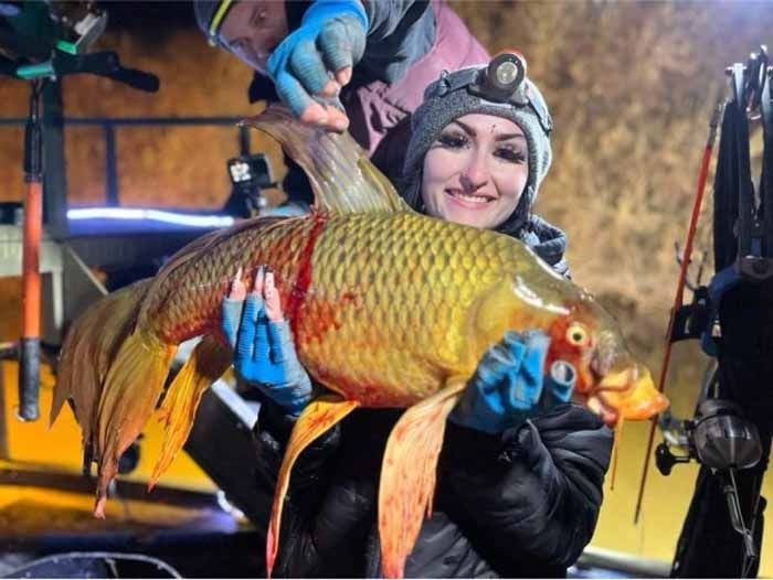 A woman is holding a large fish in her hands.