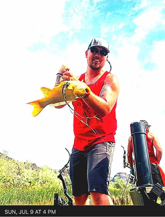 A man in a red tank top is holding a large fish