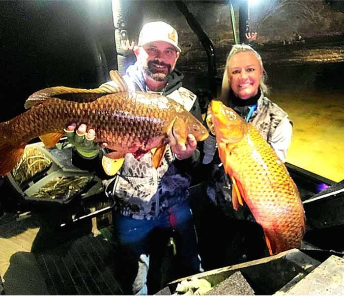 A man and a woman are holding two large fish in their hands.