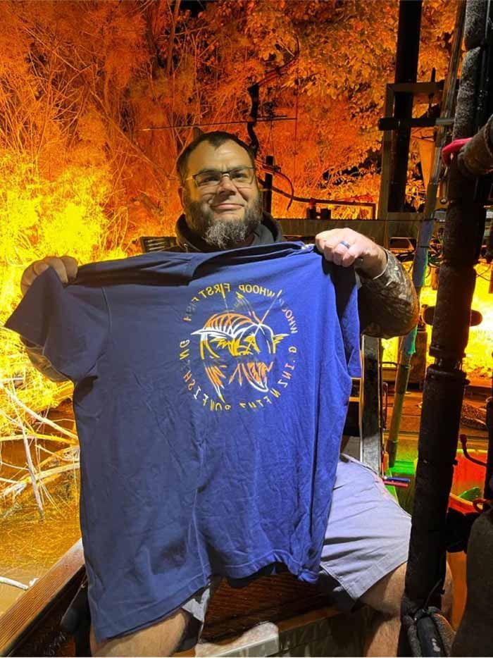 A man is holding a blue nasa t-shirt in front of a fire.