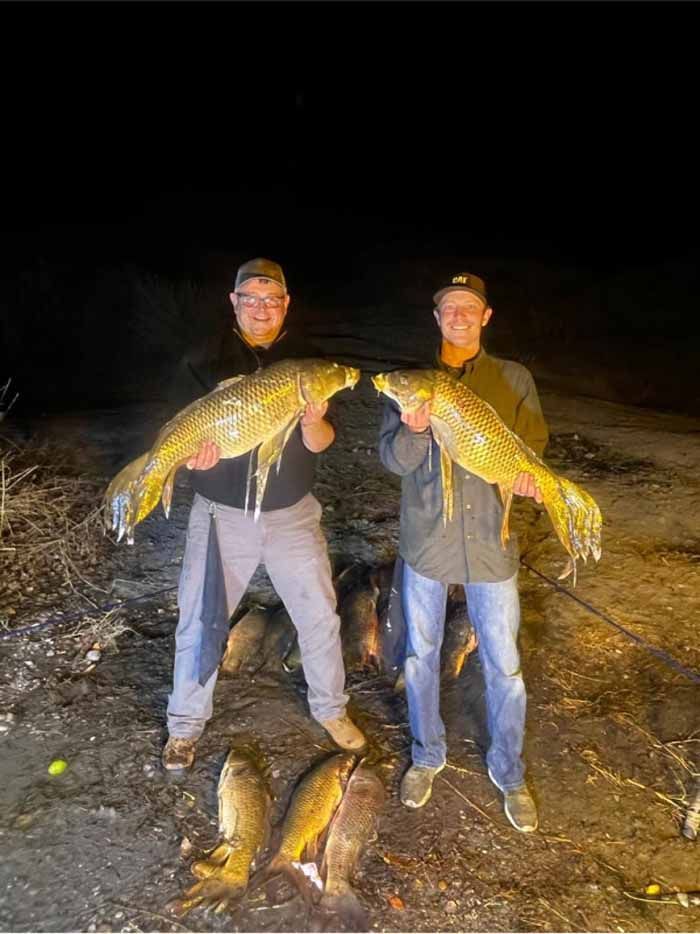 Two men are standing next to each other holding large fish.