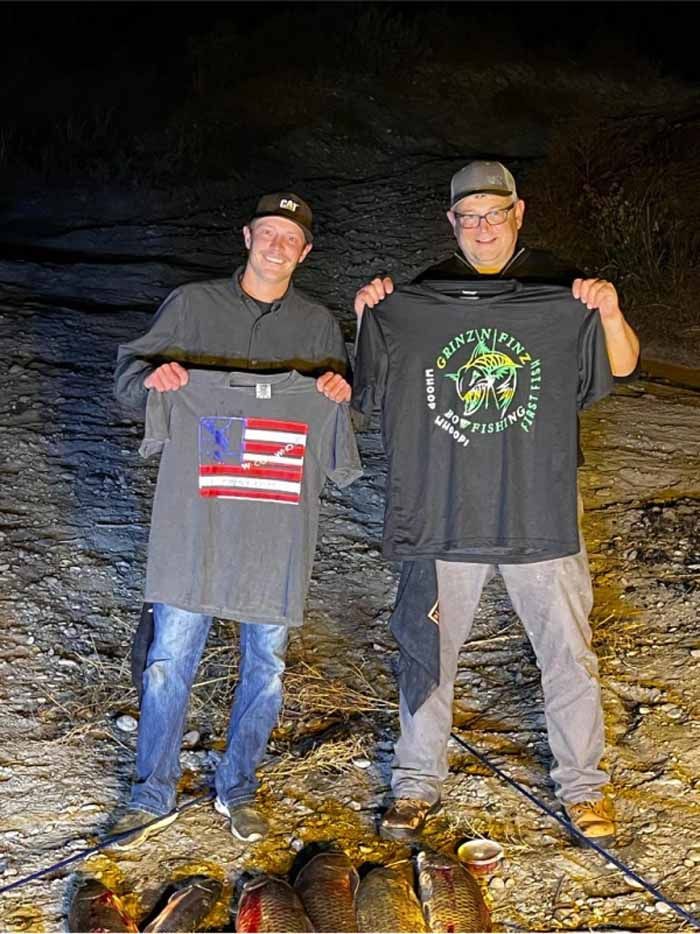 Two men standing next to each other holding up shirts one of which has an american flag on it