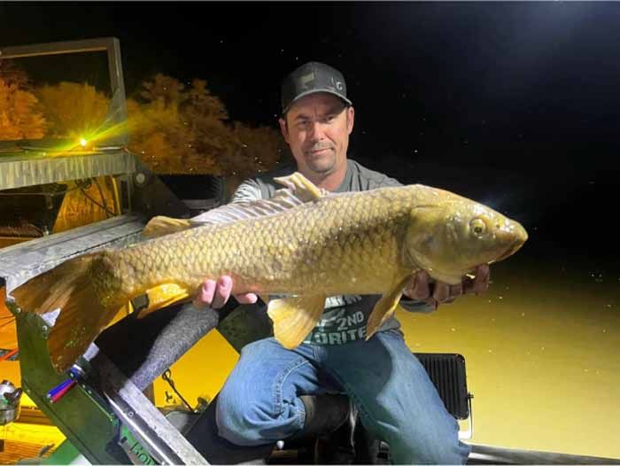 A man is sitting on a boat holding a large fish.