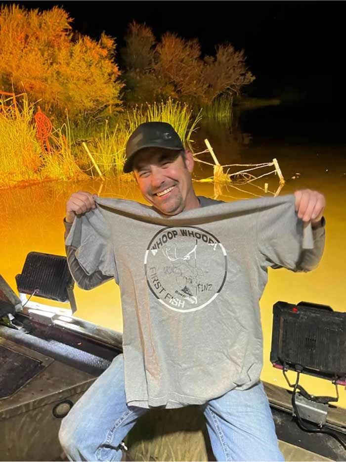 A man is standing in a boat holding a t-shirt.