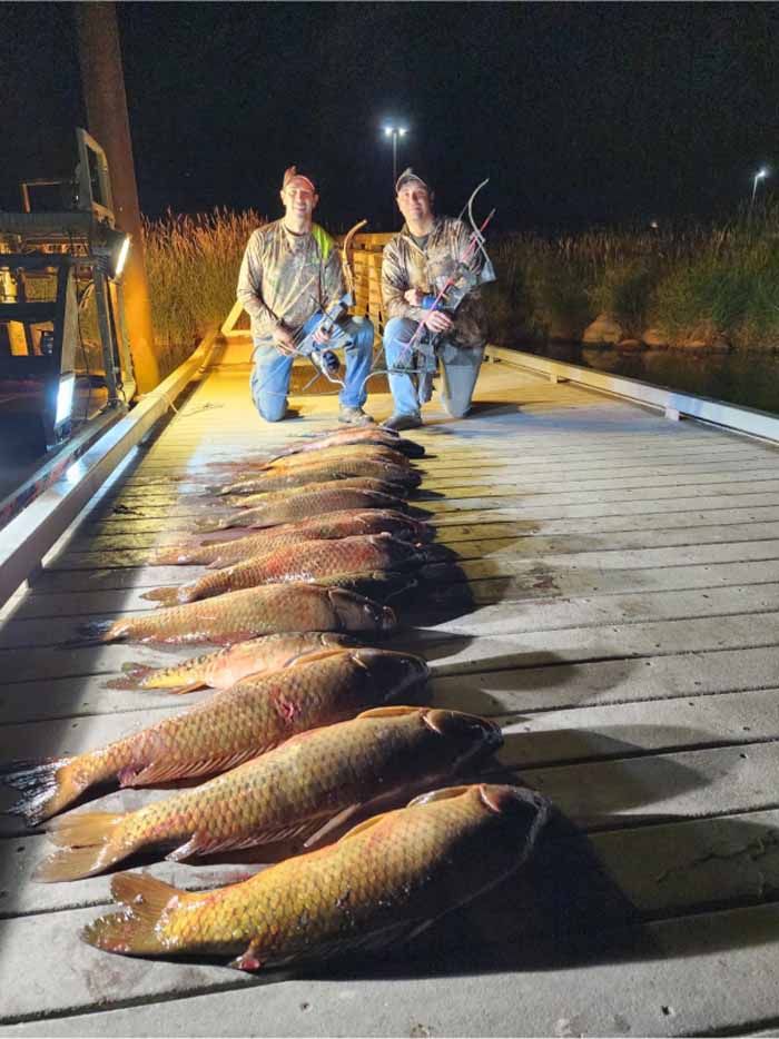 Two men are kneeling on a dock with a bunch of fish on it.