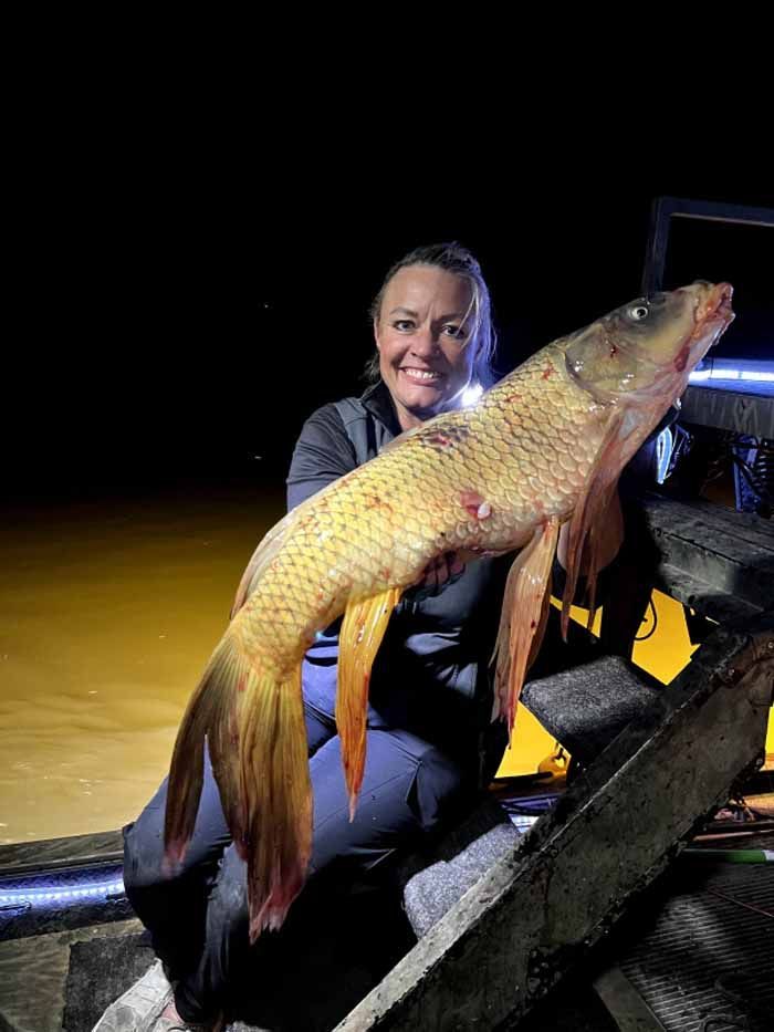 A woman is sitting on a boat holding a large carp.