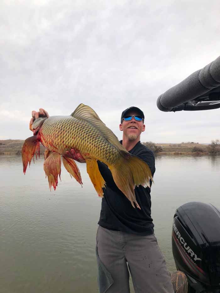 A man is holding a large fish in his hands in front of a boat.