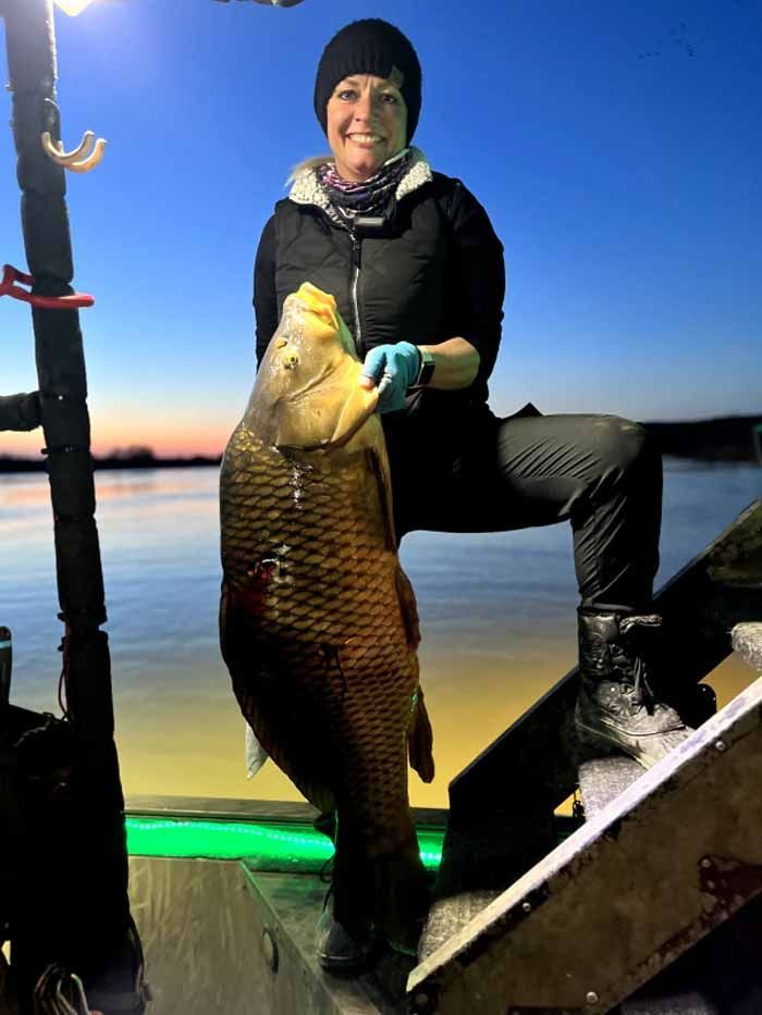 A woman is sitting on a boat holding a large fish.
