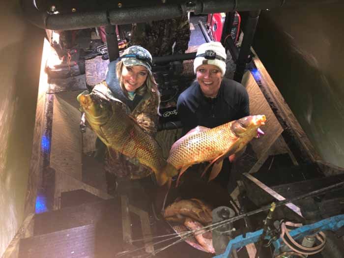 Two people are standing next to each other holding large fish.