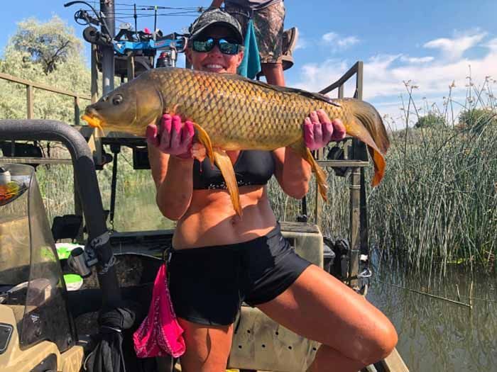 A woman is holding a large fish in her hands while standing on a boat.