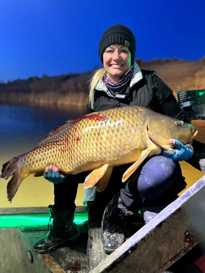 A woman is sitting in a boat holding a large carp.