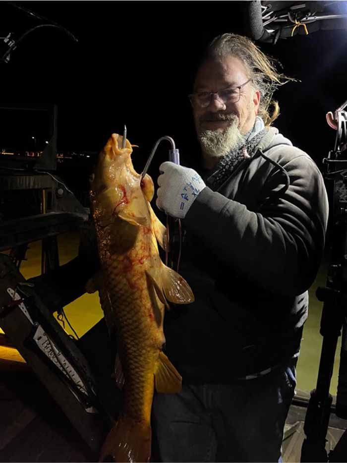 A man with a beard is holding a large fish in his hands.