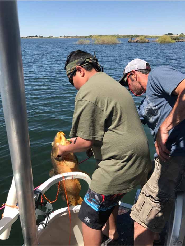 Two men are fishing on a boat and one of them is holding a fish