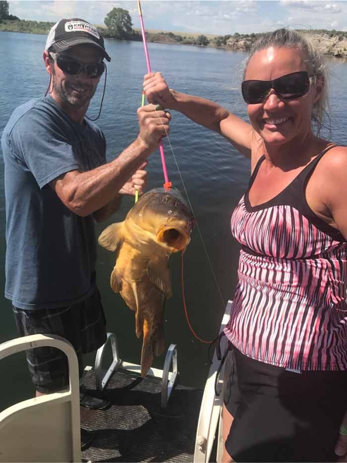 A man and a woman are standing on a boat holding a fish.