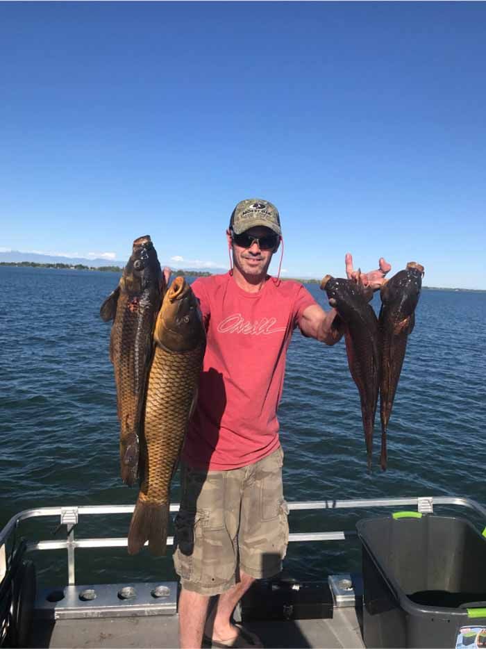 A man is standing on a boat holding three fish.