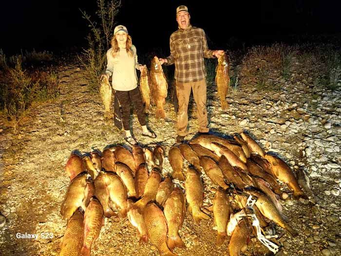 A man and a woman are standing next to a pile of fish.