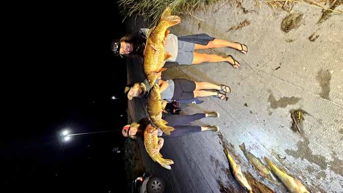 A group of people standing next to each other holding fish.