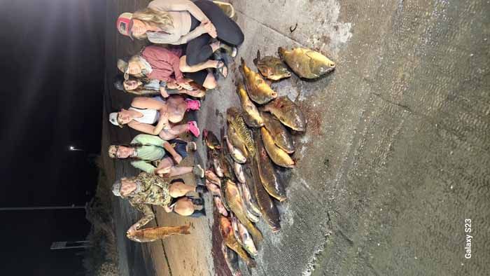 A group of people are standing next to a pile of fish.