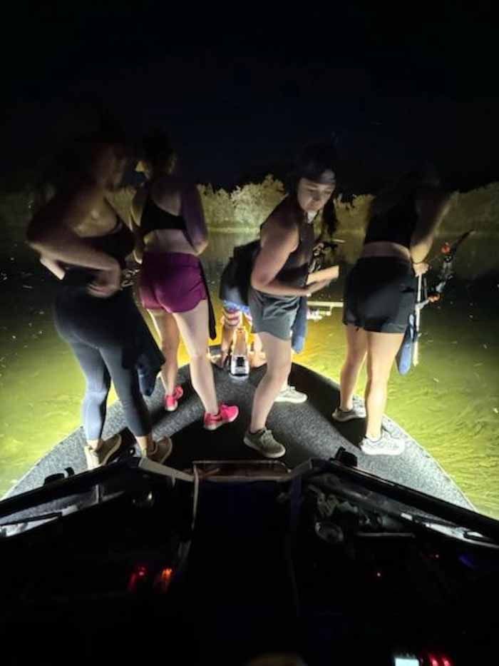 A group of women are standing on the back of a boat at night.