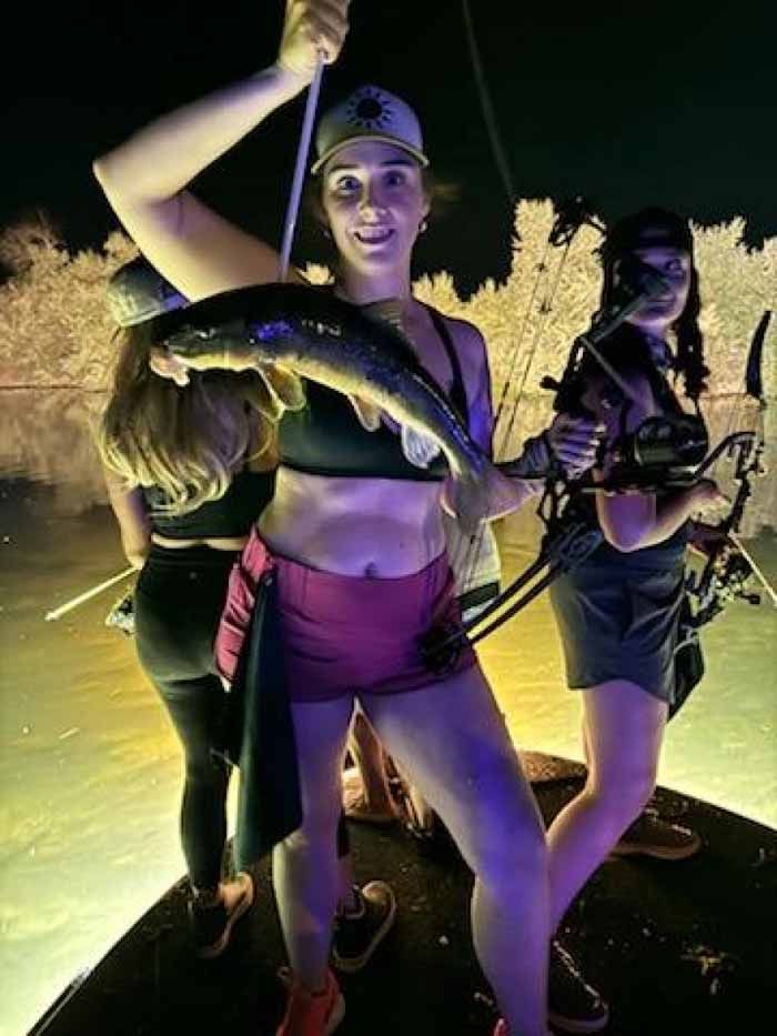 A woman is holding a fish in her hand while standing on a boat.