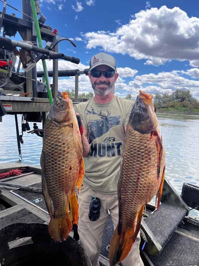 A man is holding two large fish on a boat.