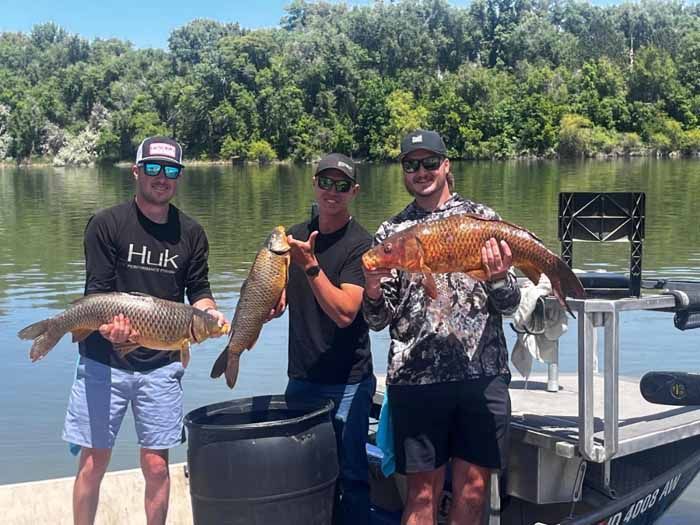 Three men are standing on a dock holding large fish.