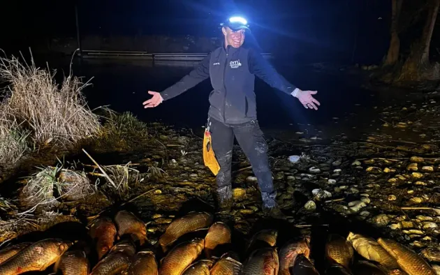 A man is standing in front of a pile of fish at night.